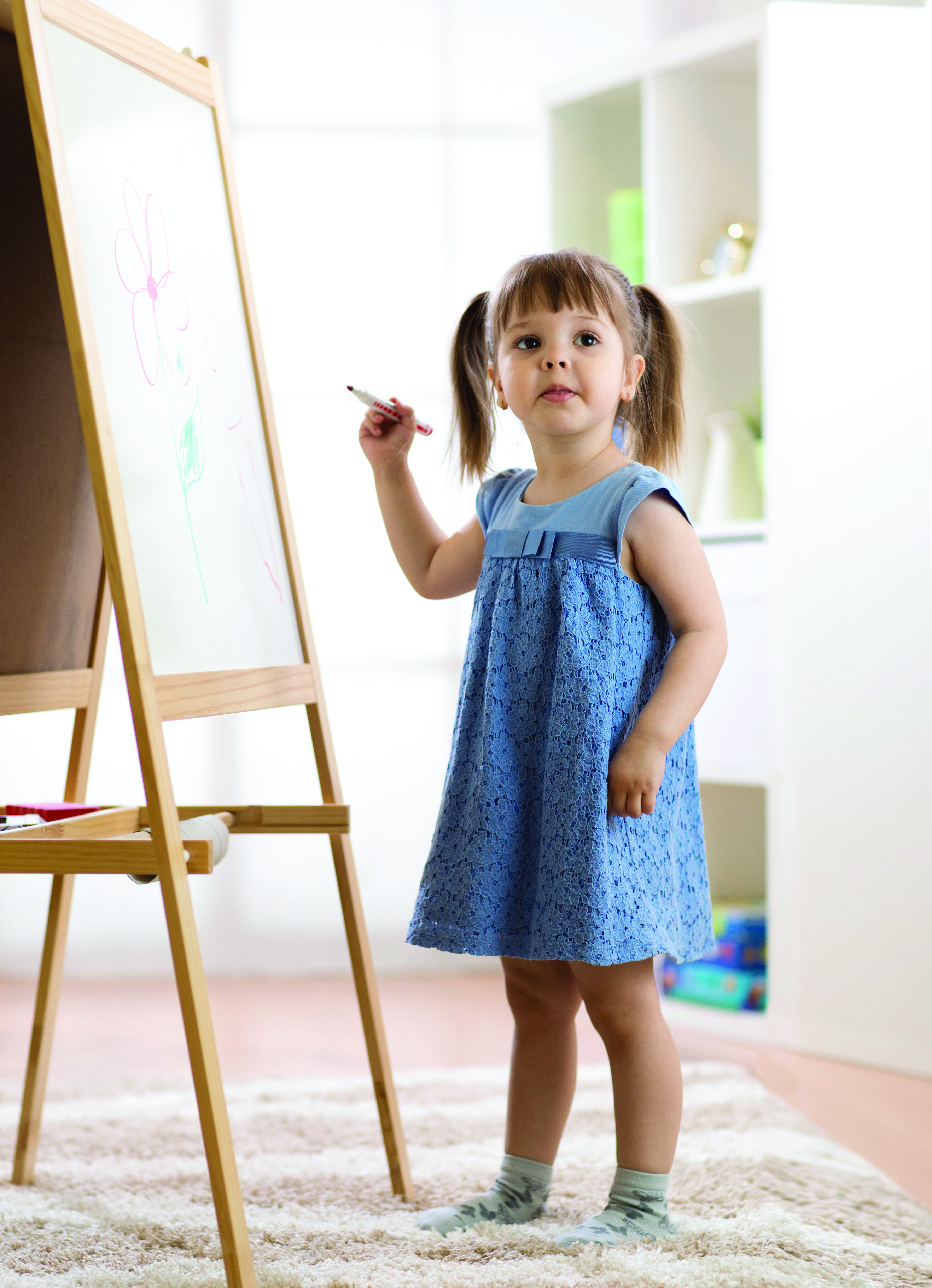 young child holding a marker standing beside an easel with a picture of a flower drawn on it